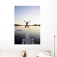 A swimmer jumps off a diving board as the sun sets over a lake Wall Mural