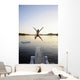 A swimmer jumps off a diving board as the sun sets over a lake Wall Mural