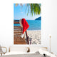 Red Santa's hat hanging on beach chair under palm tree Wall Mural