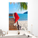 Red Santa's hat hanging on beach chair under palm tree Wall Mural