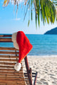 Red Santa's hat hanging on beach chair under palm tree Wall Mural