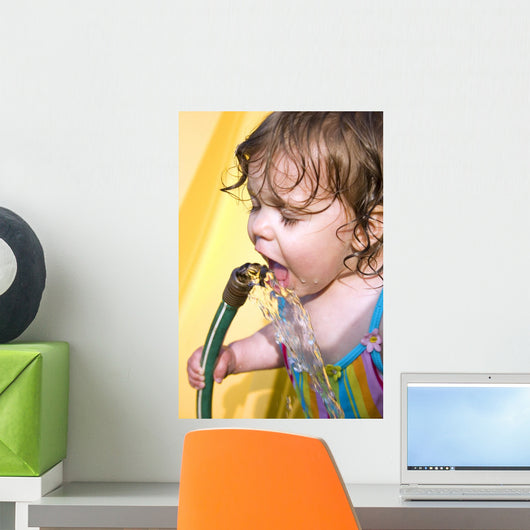 a toddler drinking water from a garden hose Wall Mural