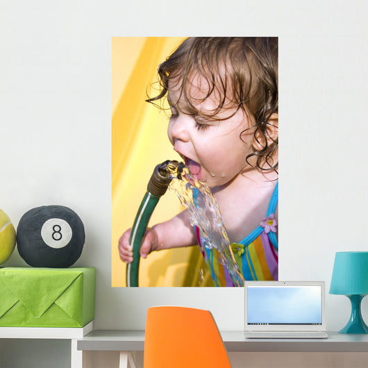 a toddler drinking water from a garden hose Wall Mural