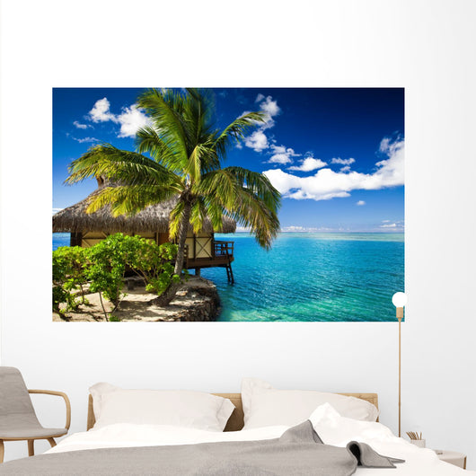 Tropical bungalow and palm tree next to amazing lagoon Wall Mural