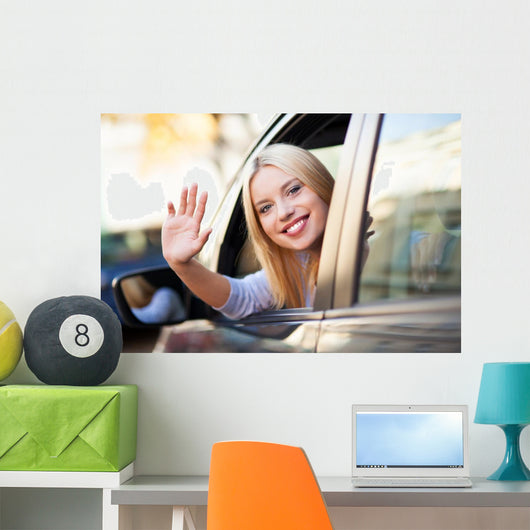 Young woman waving from car window Wall Mural