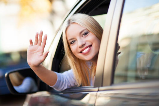 Young woman waving from car window Wall Mural
