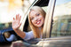 Young woman waving from car window Wall Mural