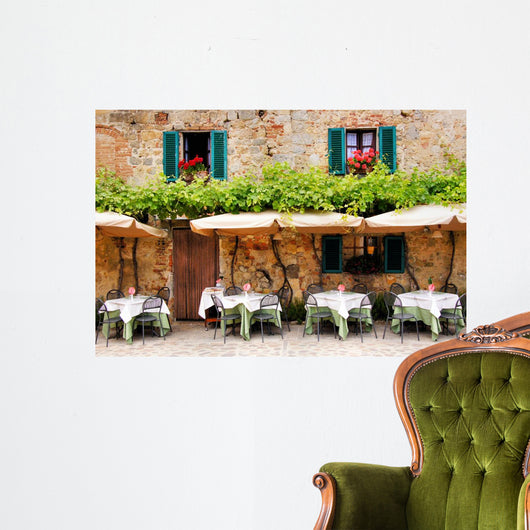 Cafe tables and chairs outside a stone building in Tuscany Wall Mural