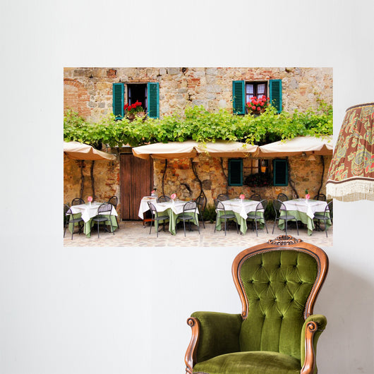 Cafe tables and chairs outside a stone building in Tuscany Wall Mural