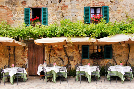 Cafe tables and chairs outside a stone building in Tuscany Wall Mural