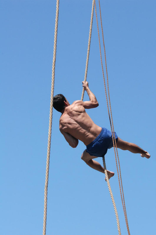 Shirtless athlete climbing up the rope Wall Mural