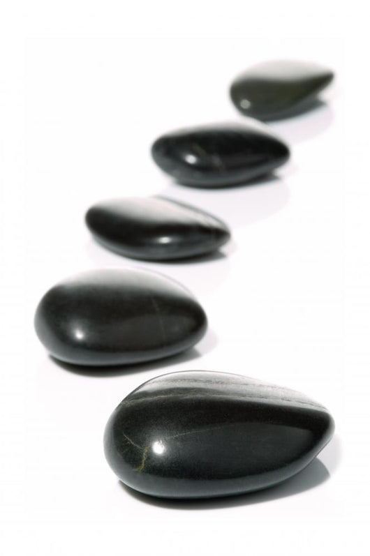 Five black pebbles in a gentle curve on a white surface Wall Mural