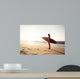 Beautiful surfer girl in the beach with her surfboard at sunset Wall Mural