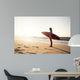 Beautiful surfer girl in the beach with her surfboard at sunset Wall Mural