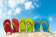 Row of colorful flip flops on beach against sunny sky 