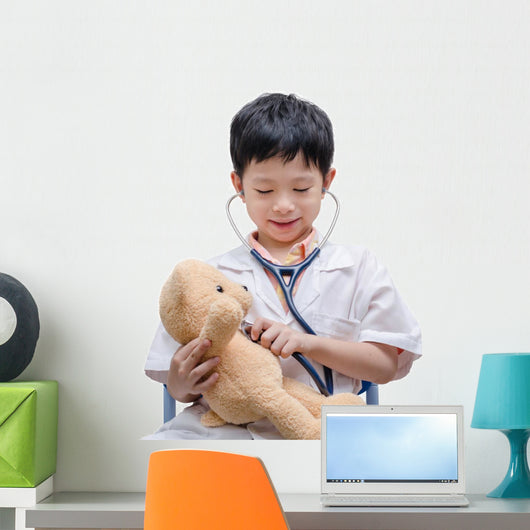 Young Asian doctor boy playing and curing bear toy isolated on w Wall Decal