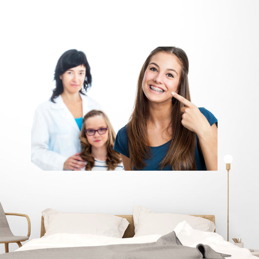 Teen girl pointing at dental barces with doctor in background. Wall Mural