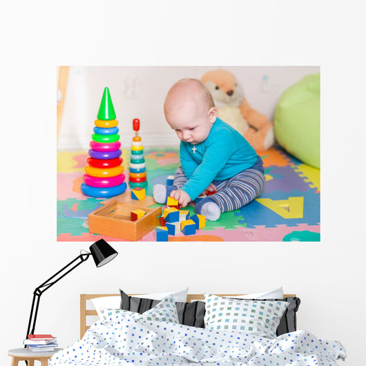 Cute little baby playing with colorful toys indoors Wall Mural