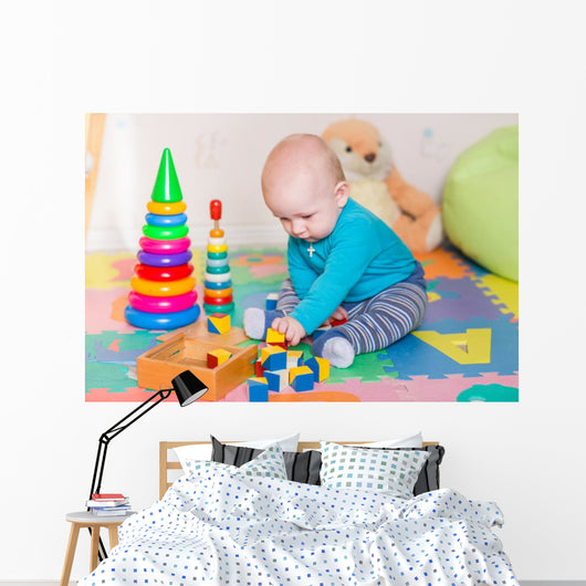 Cute little baby playing with colorful toys indoors Wall Mural