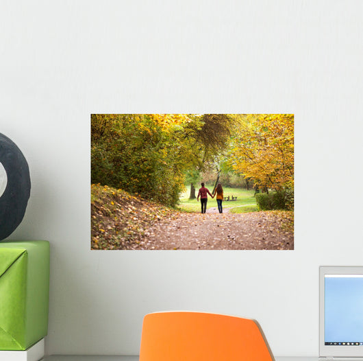 Young love couple, holding hands walking in the autumn forest Wall Mural