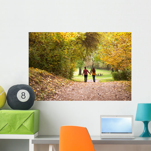 Young love couple, holding hands walking in the autumn forest Wall Mural