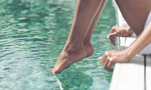 Young Woman Sitting at Poolside with Toes on Water Wall Mural
