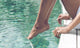 Young Woman Sitting at Poolside with Toes on Water Wall Mural