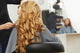 Blonde curly hair. Hairdresser doing hairstyle for young woman i Wall Mural