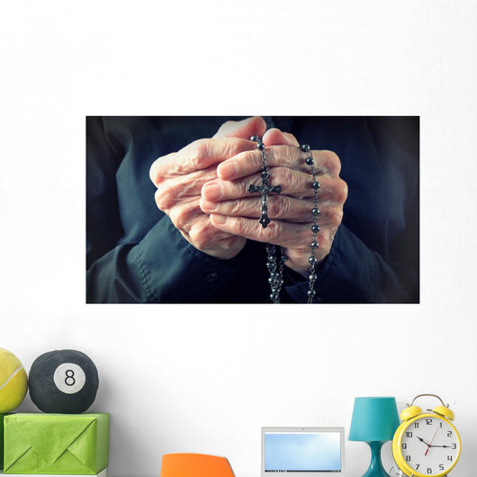 Hands of an elder woman holding a rosary while praying Wall Mural