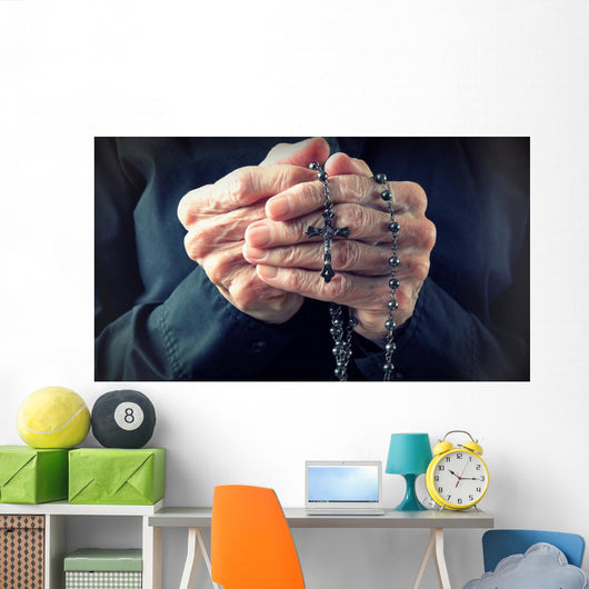 Hands of an elder woman holding a rosary while praying Wall Mural