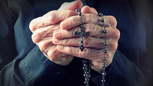 Hands of an elder woman holding a rosary while praying Wall Mural