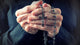 Hands of an elder woman holding a rosary while praying Wall Mural