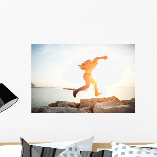 brave man running over rocks near ocean in beautiful sunset Wall Decal