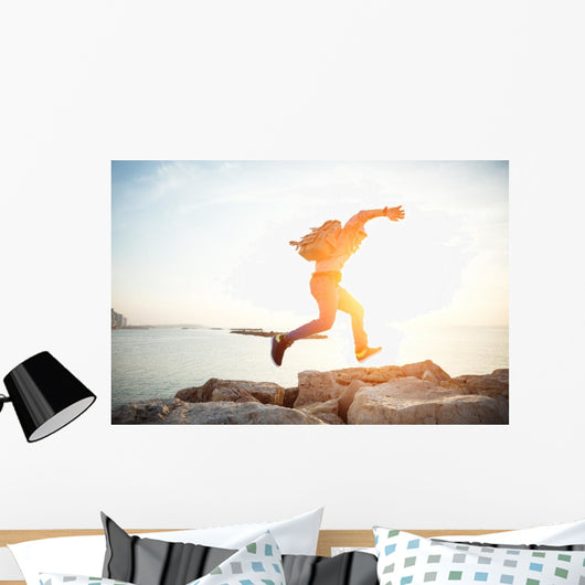brave man running over rocks near ocean in beautiful sunset Wall Decal