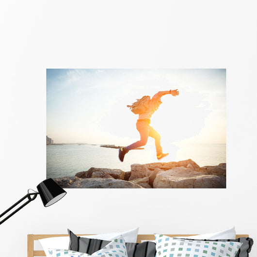 brave man running over rocks near ocean in beautiful sunset Wall Decal