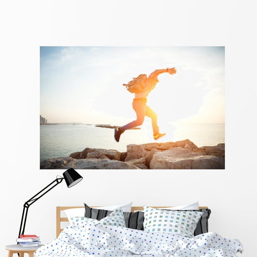 brave man running over rocks near ocean in beautiful sunset Wall Decal