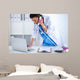 Young woman doctor in white coat at computer using phone Wall Decal