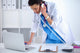 Young woman doctor in white coat at computer using phone Wall Decal