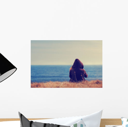 Girl sitting on a meadow with a beautiful sea/ocean view. Wall Decal