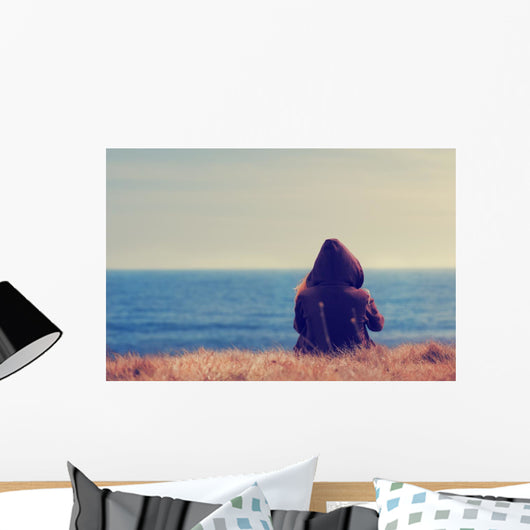 Girl sitting on a meadow with a beautiful sea/ocean view. Wall Decal
