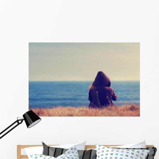 Girl sitting on a meadow with a beautiful sea/ocean view. Wall Decal