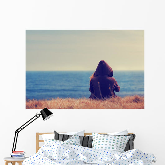 Girl sitting on a meadow with a beautiful sea/ocean view. Wall Decal