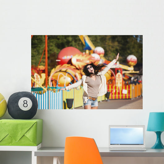 Amusement park rides. A young woman is happy and jumps. Wall Mural