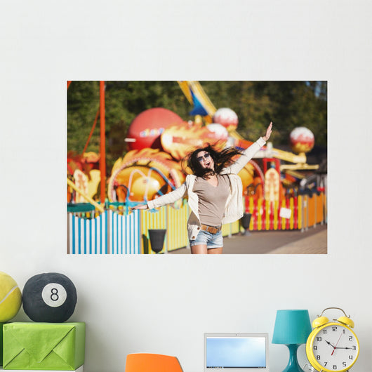 Amusement park rides. A young woman is happy and jumps. Wall Mural