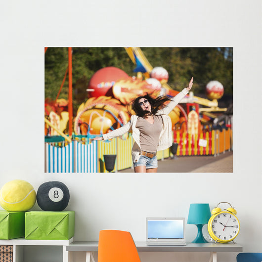 Amusement park rides. A young woman is happy and jumps. Wall Mural