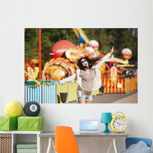 Amusement park rides. A young woman is happy and jumps. Wall Mural