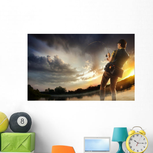 Young man fishing at dramatic sunset Wall Mural