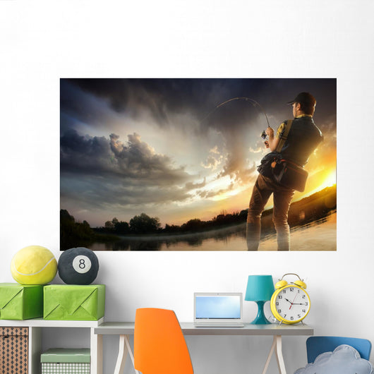 Young man fishing at dramatic sunset Wall Mural