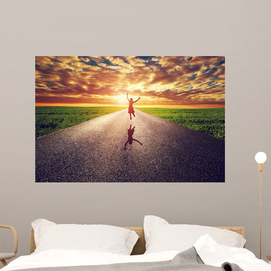 Happy woman jumping on long straight road, way towards sun Wall Mural