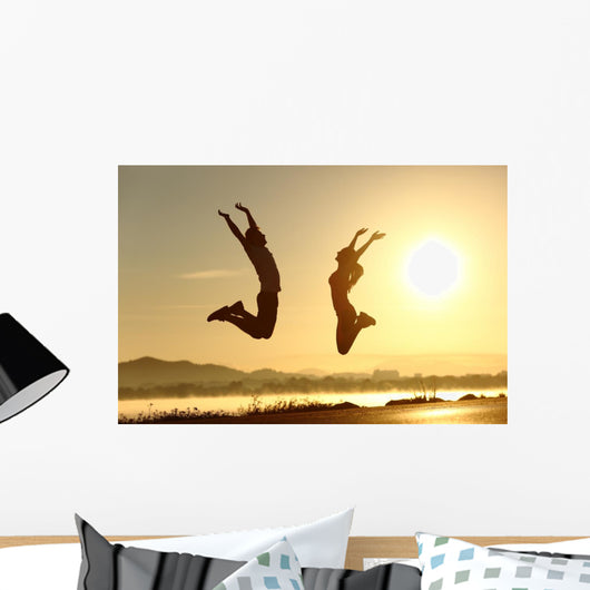 Fitness couple jumping happy at sunset Wall Mural
